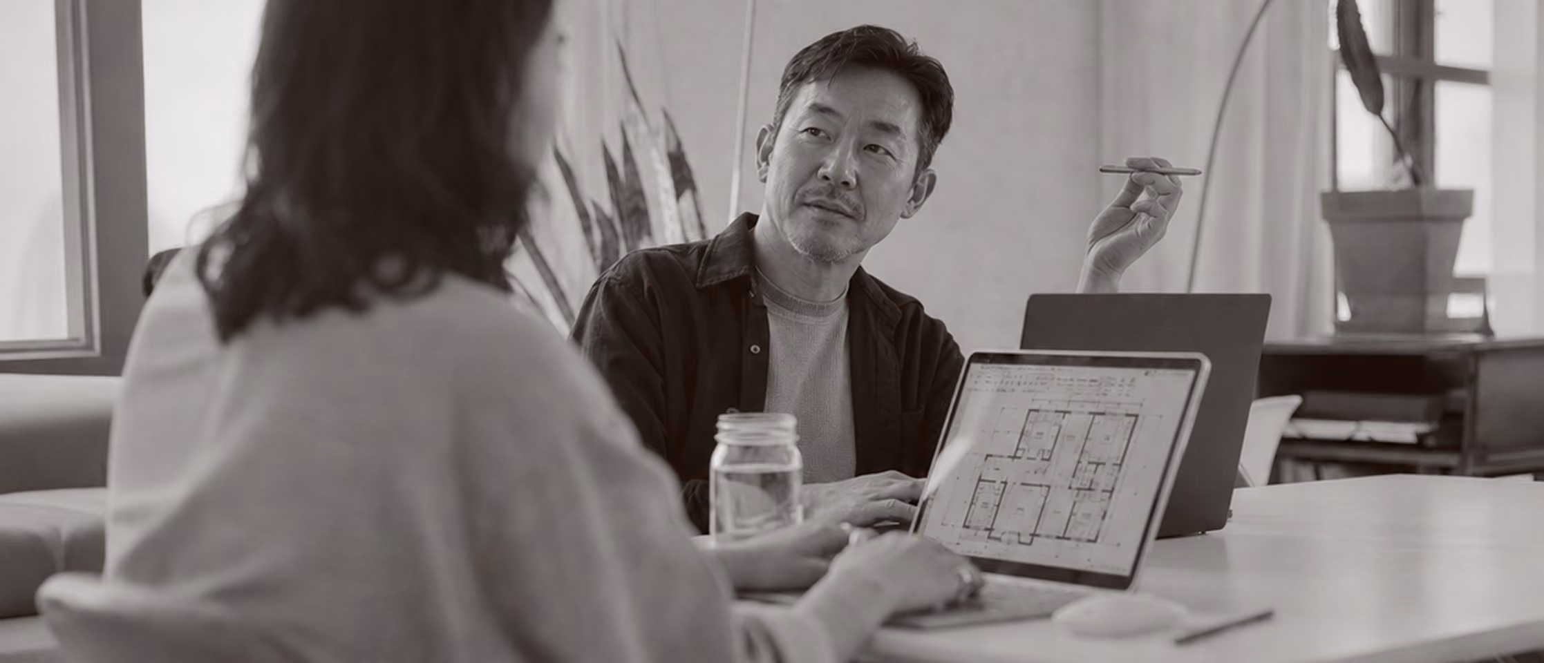 Two people discussing architectural plans on a laptop in a bright office setting.