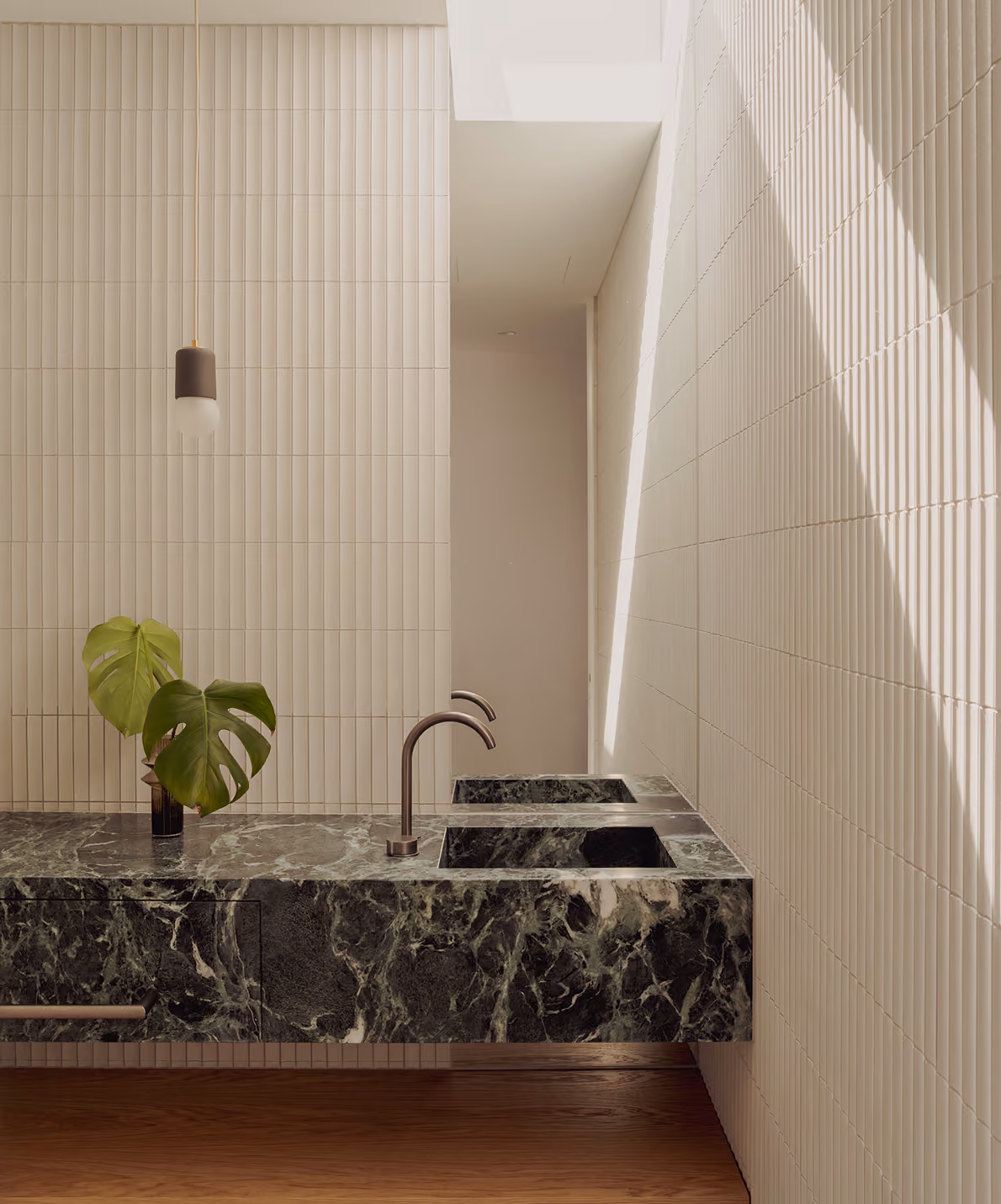 Modern bathroom with green marble floating sink, sleek faucets, textured white tile walls, and wooden floor.