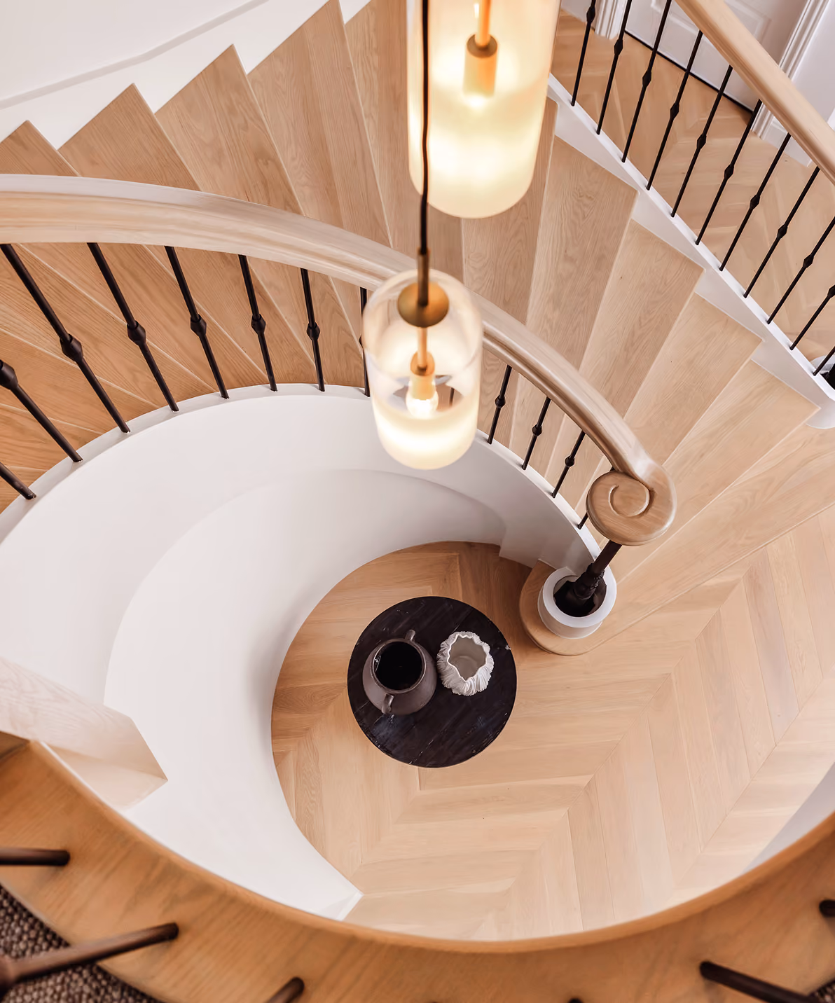 Top view of a wooden spiral staircase with black balusters and two hanging pendant lights.