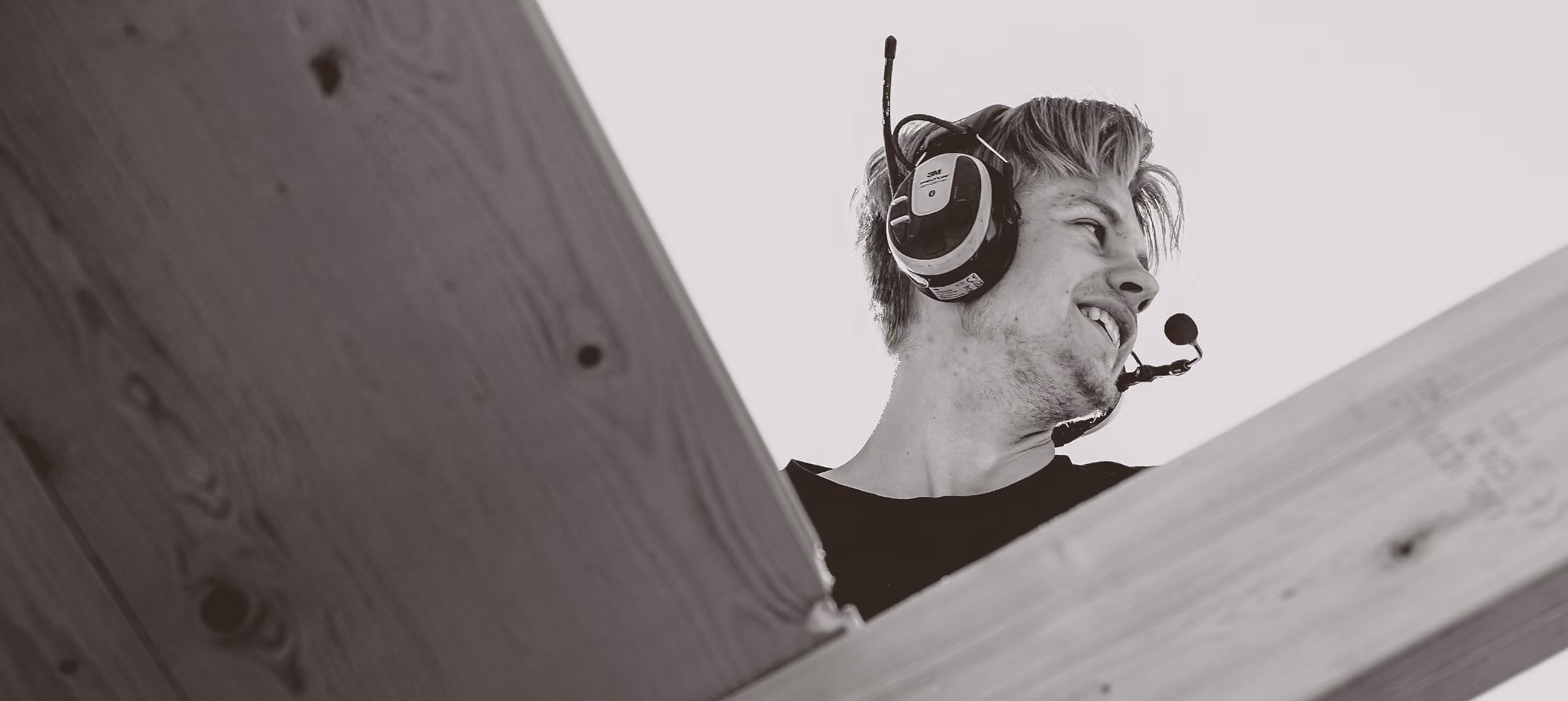 Young man smiling while wearing a headset with microphone behind wooden beams.