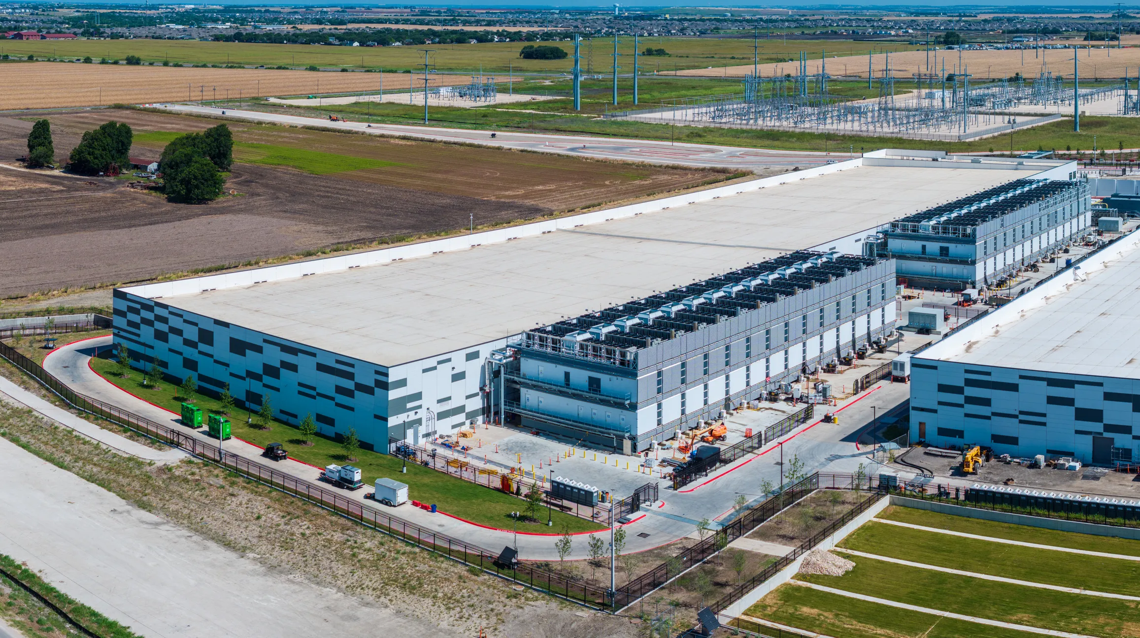 Aerial view of a large, modern data center with cooling units on the roof in a rural area.