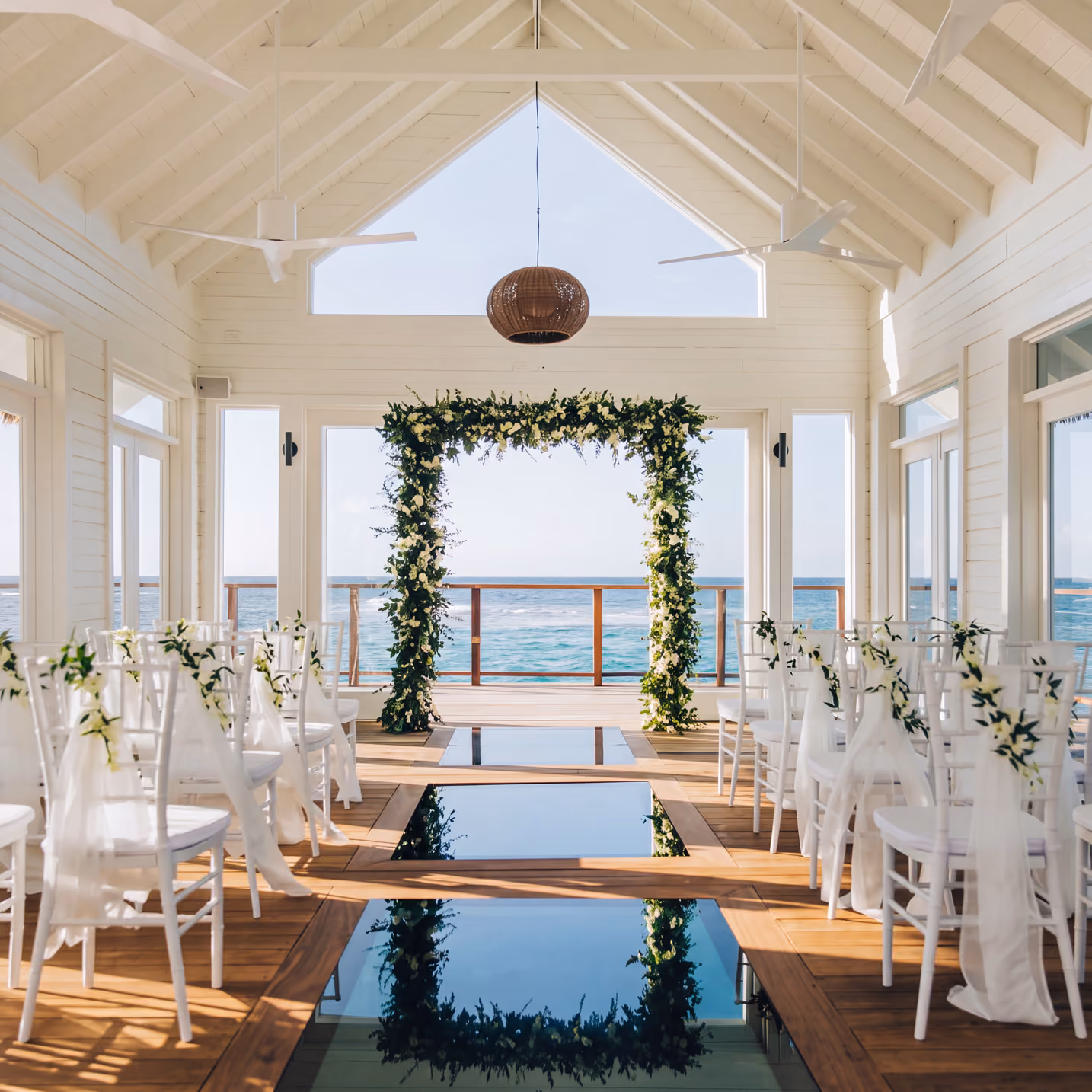 Oceanfront wedding pavilion with white chairs and a floral arch set up for a destination wedding ceremony.
