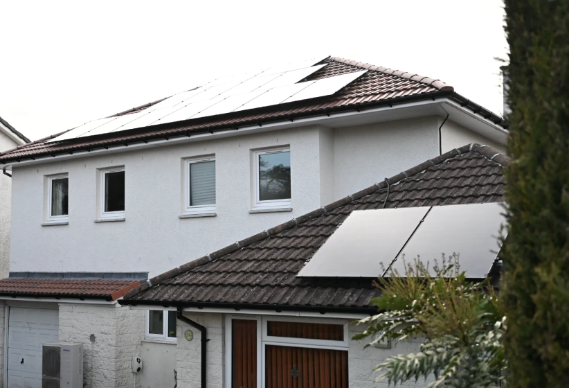 White two-story house with solar panels installed on its tiled roof.
