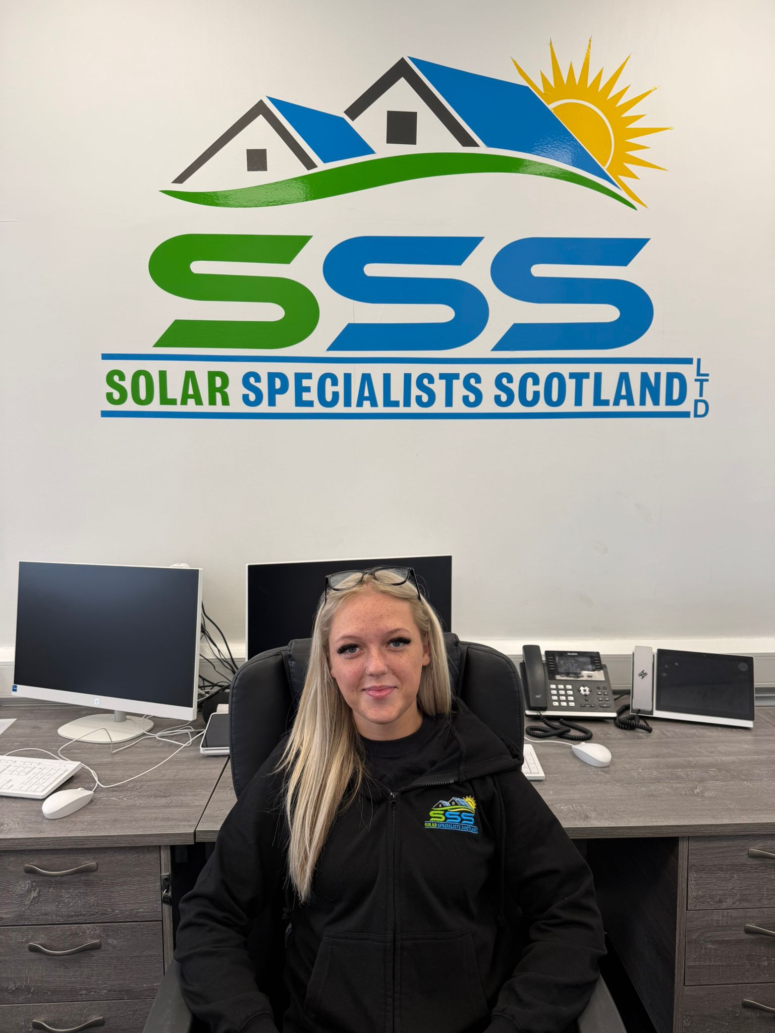 Woman with long blonde hair sitting in office chair under Solar Specialists Scotland logo.