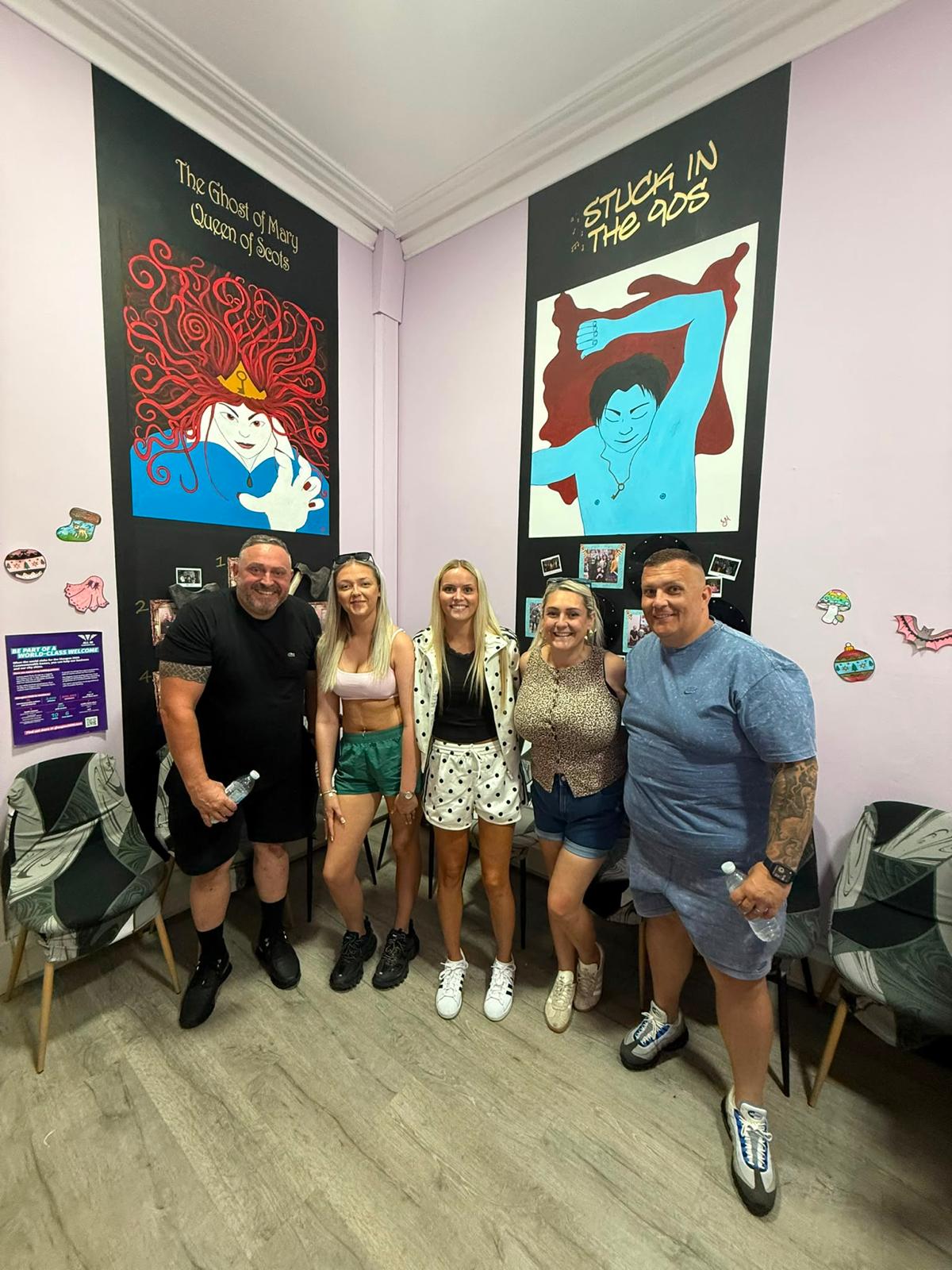 Five people standing indoors between two colorful wall murals, smiling at the camera.