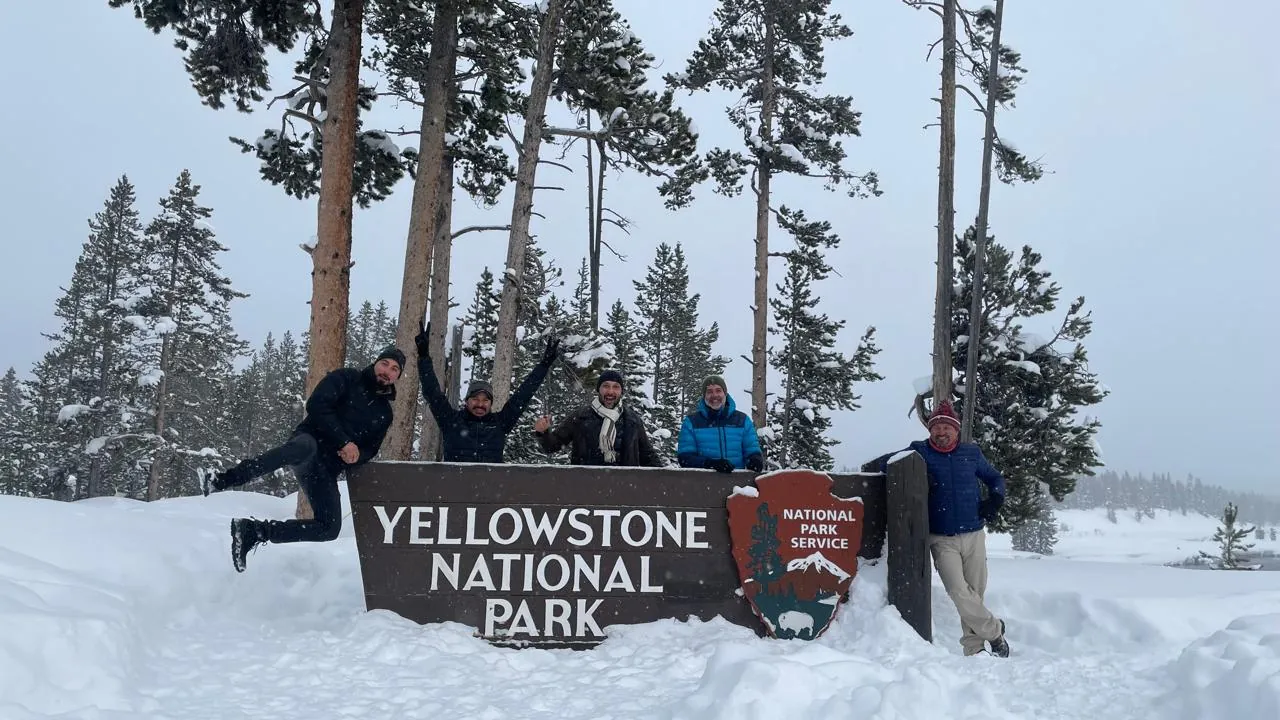 Grupo del club saltando junto al cartel del Parque Nacional Yellowstone nevado