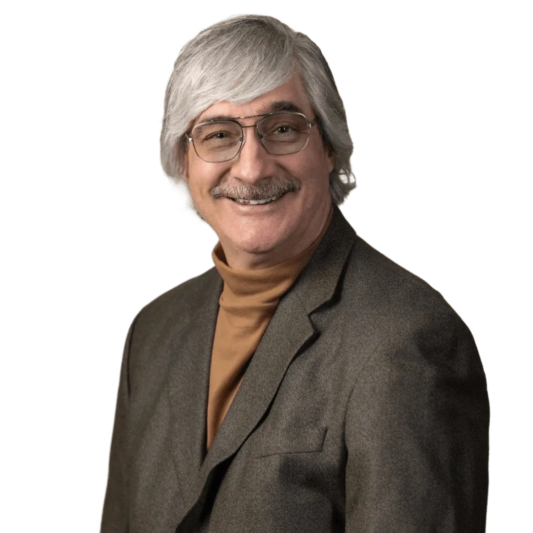 Smiling middle-aged man with gray hair and mustache, wearing glasses, a brown turtleneck, and a dark blazer.