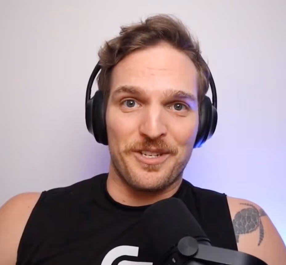 Man with headphones speaking into a microphone with a tattoo of a turtle on his shoulder.