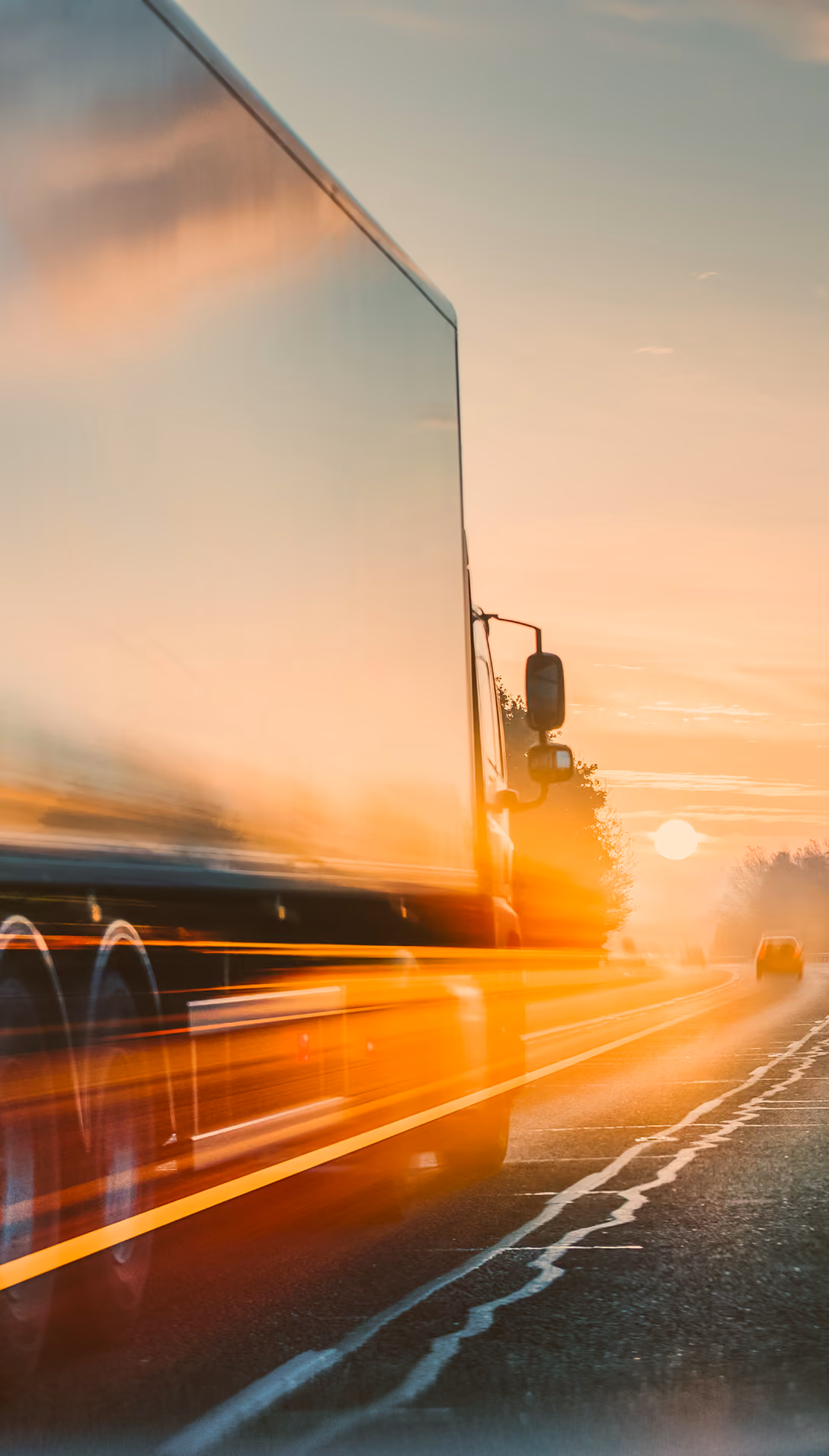 Side view of a large truck driving on a road at sunset with motion blur effects.