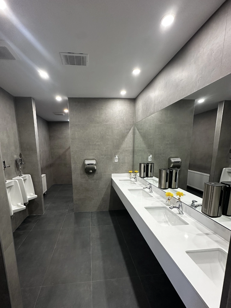 Finished commercial washroom renovation in the GTA — grey large-format tile, white quartz vanity with multiple sinks and urinals.