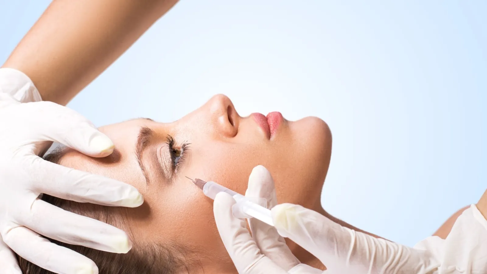 Gloved hands injecting the face of a person lying down.