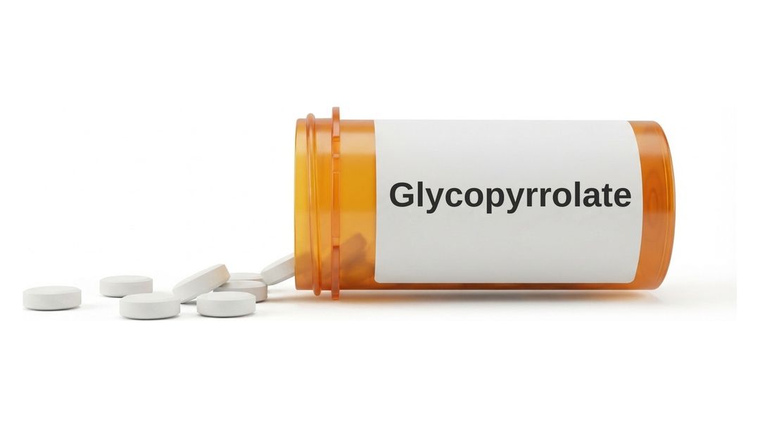 An amber prescription bottle lying on its side on a white background with a plain white label reading Glycopyrrolate, and six small round white tablets spilled out in front of it.