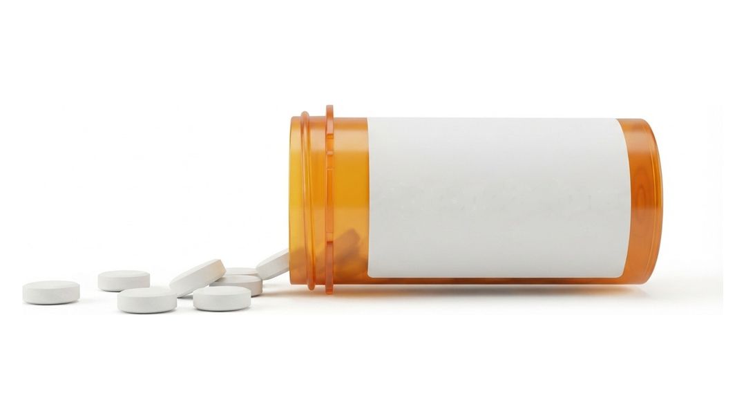 An amber prescription bottle lying on its side on a white background with a blank white label and no name on it, and six small round white tablets spilled out in front of it.