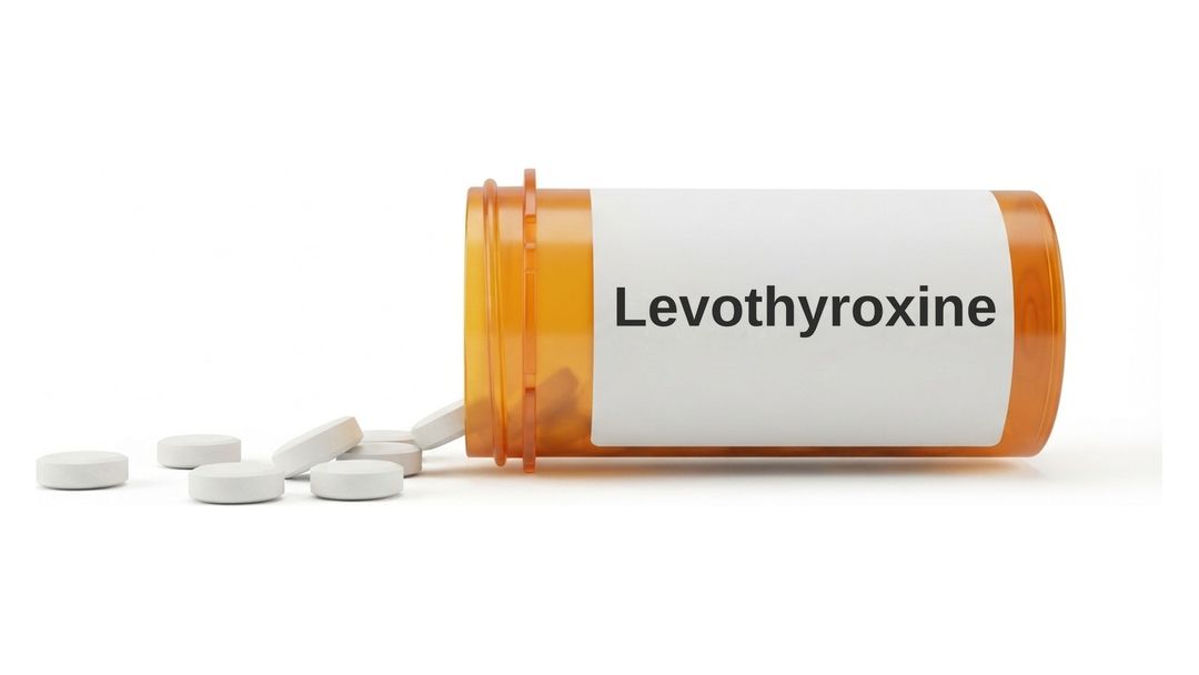 An amber prescription bottle lying on its side on a white background with a plain white label reading Levothyroxine, and six small round white tablets spilled out in front of it.