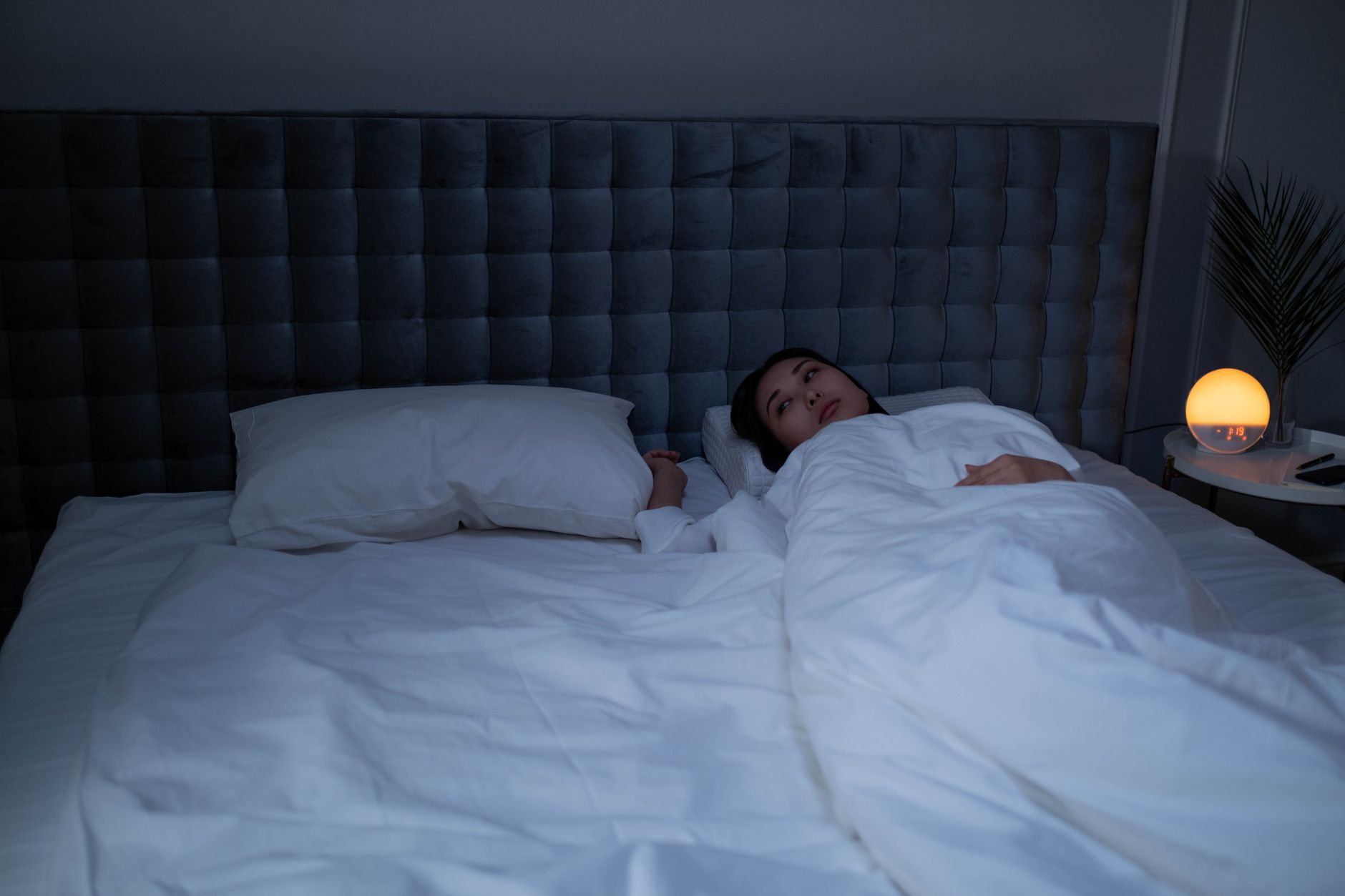 A person lying awake in a dark bedroom scratching one arm, showing the night-time itch that costs people with eczema their sleep.