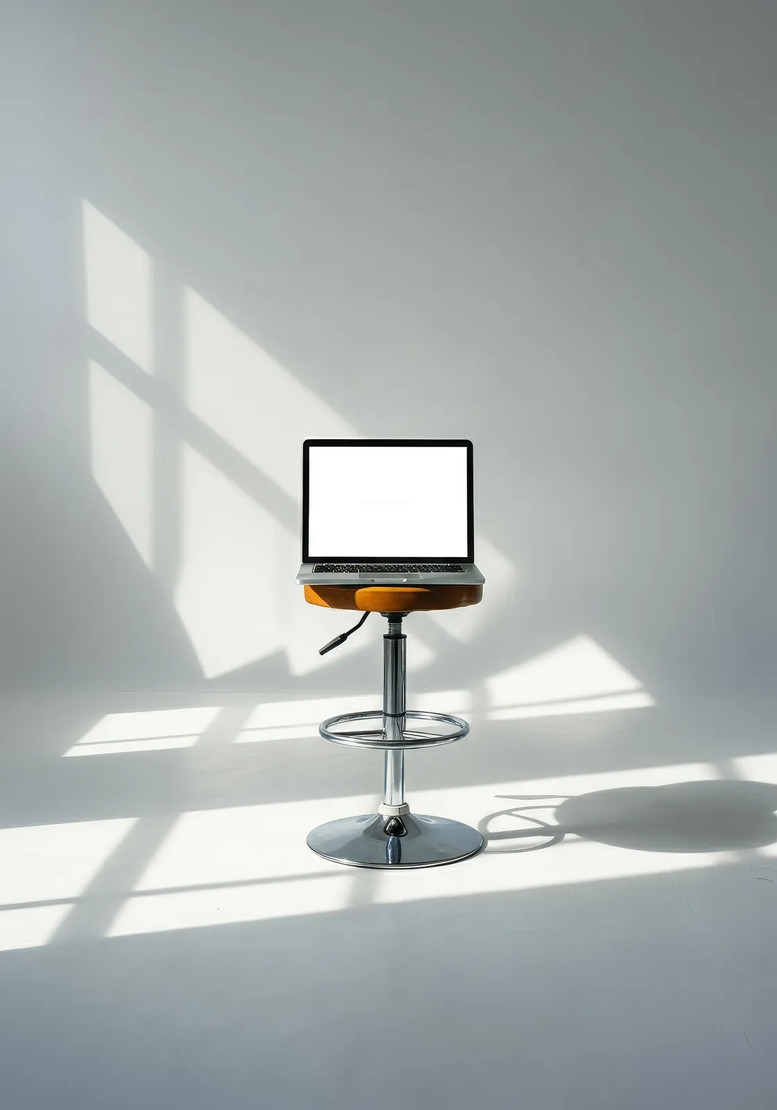 Laptop with blank white screen on a bar stool in a bright room with window shadows.