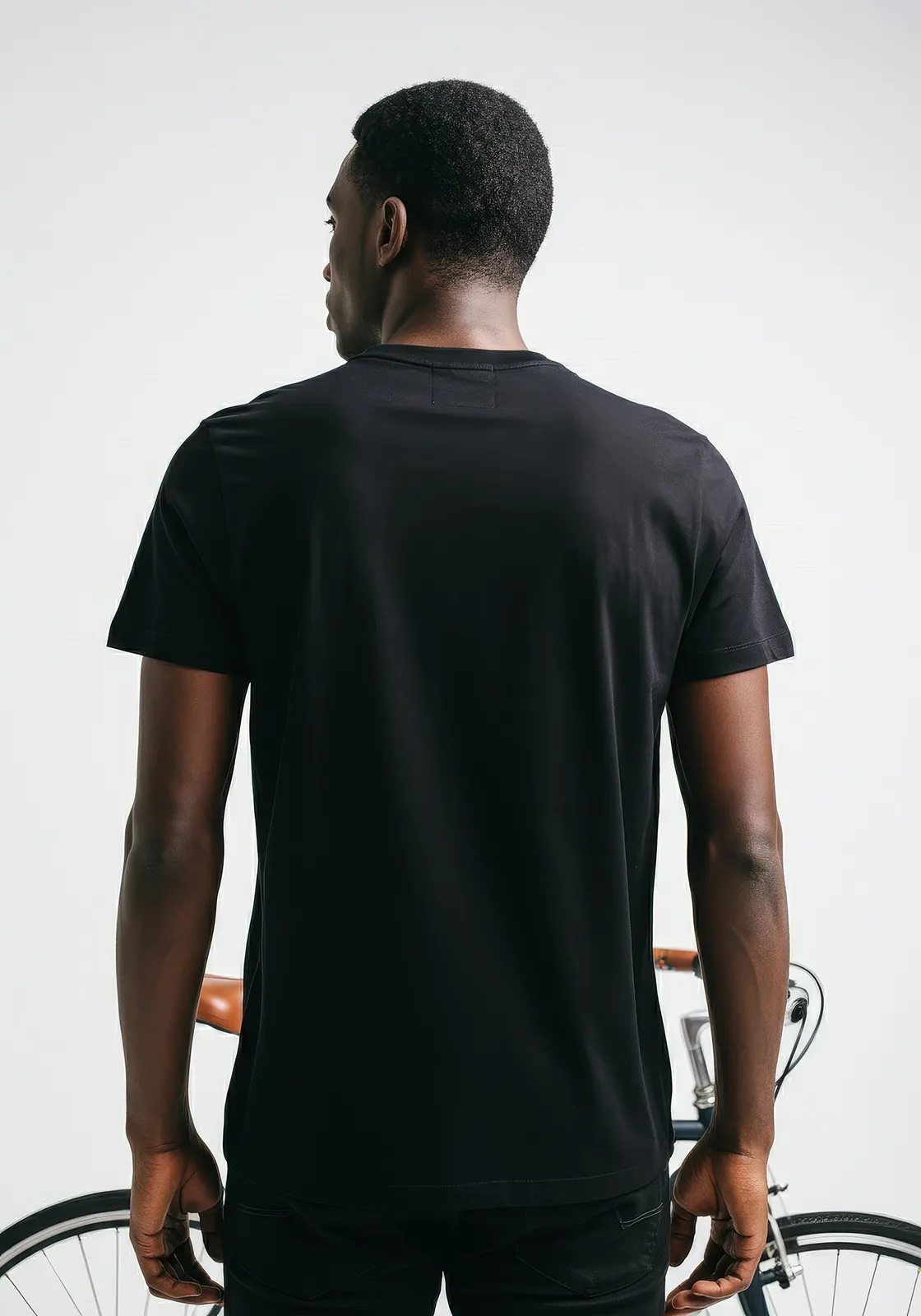 Rear view of a man in a black t-shirt standing in front of a bicycle with white background.