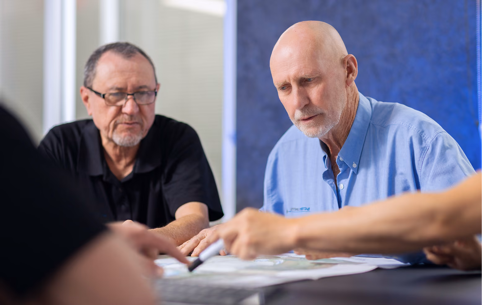 Two older men focused on a discussion while looking at papers on a table.