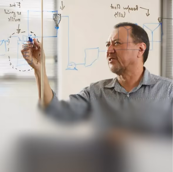 Man writing and drawing diagrams on a transparent board with blue and black markers.