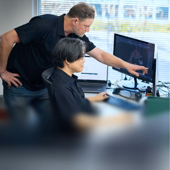 Two men collaborating at a desk with a computer showing 3D modeling software in a modern office.