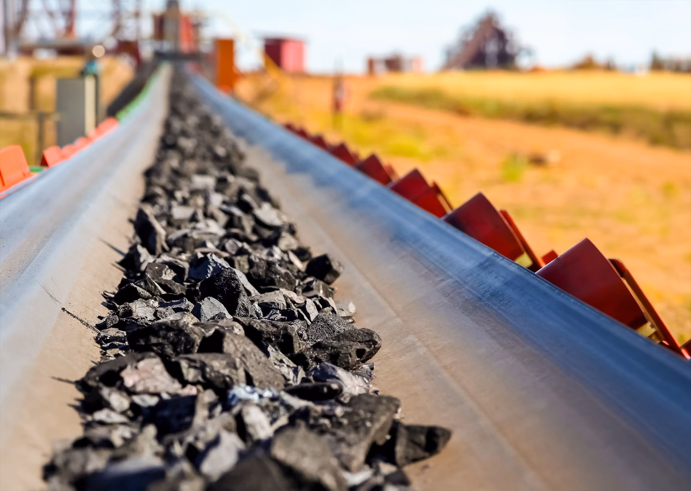 Close-up of black coal pieces moving on a conveyor belt at a mining site.