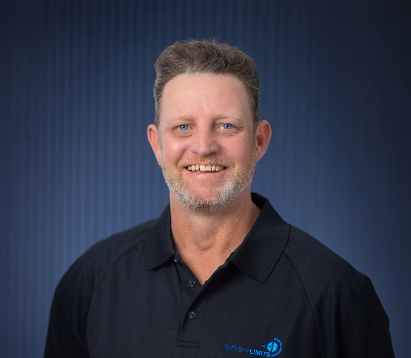 Smiling man with short gray hair and beard wearing a black Battery Limits polo shirt.