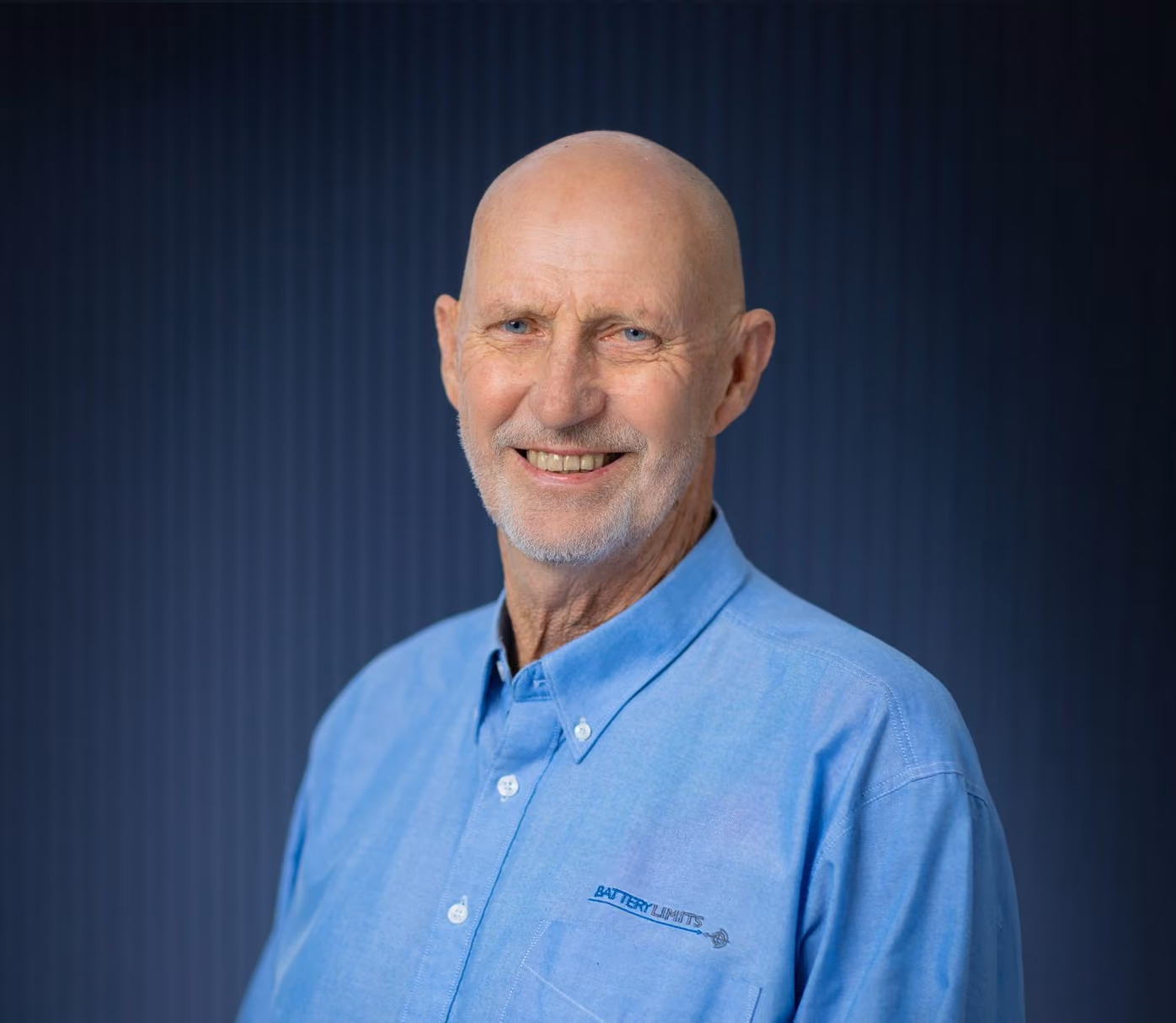 Smiling older man with a bald head and beard wearing a blue shirt with a Battery Limits logo.