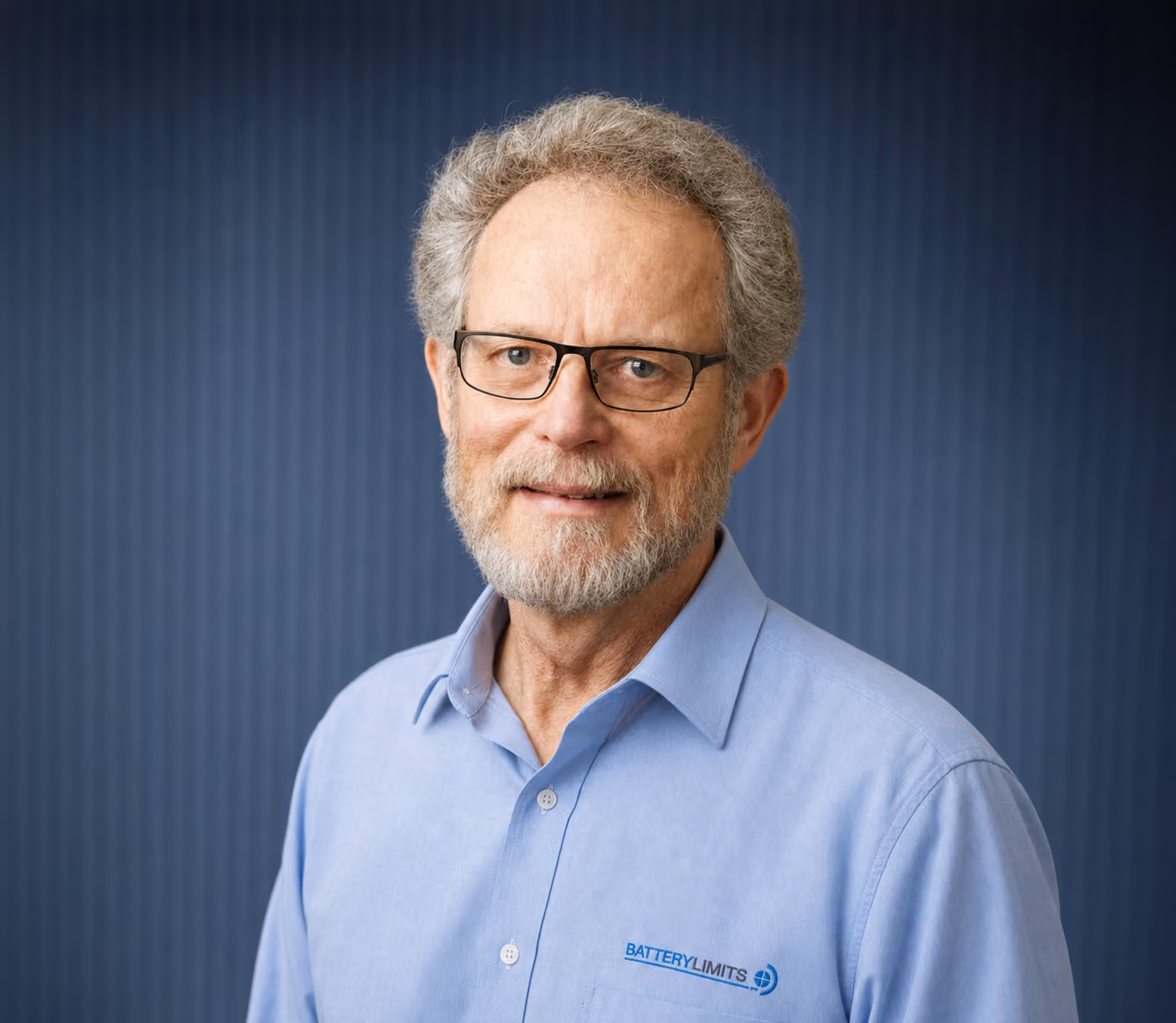 Older man with glasses and gray hair smiling, wearing a light blue Battery Limits shirt.