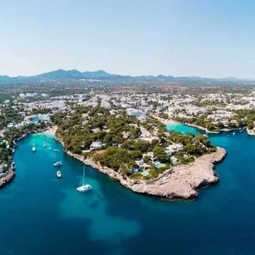 Aerial view of a coastal area with boats, clear turquoise waters, rocky shore, and scattered houses among trees Image.