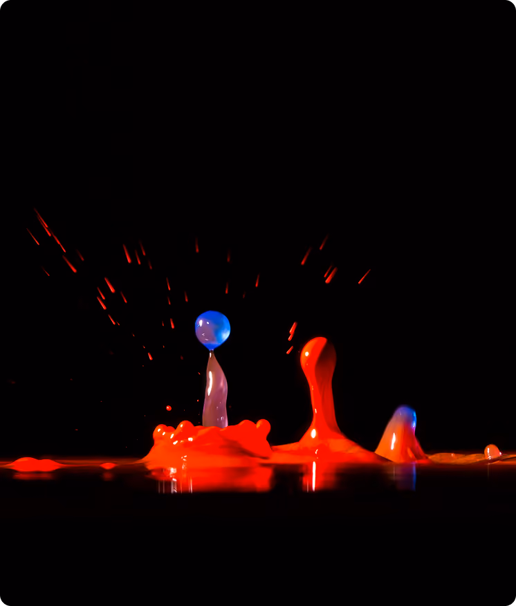 Red and blue liquid splash droplets rising against a black background in high-speed capture.