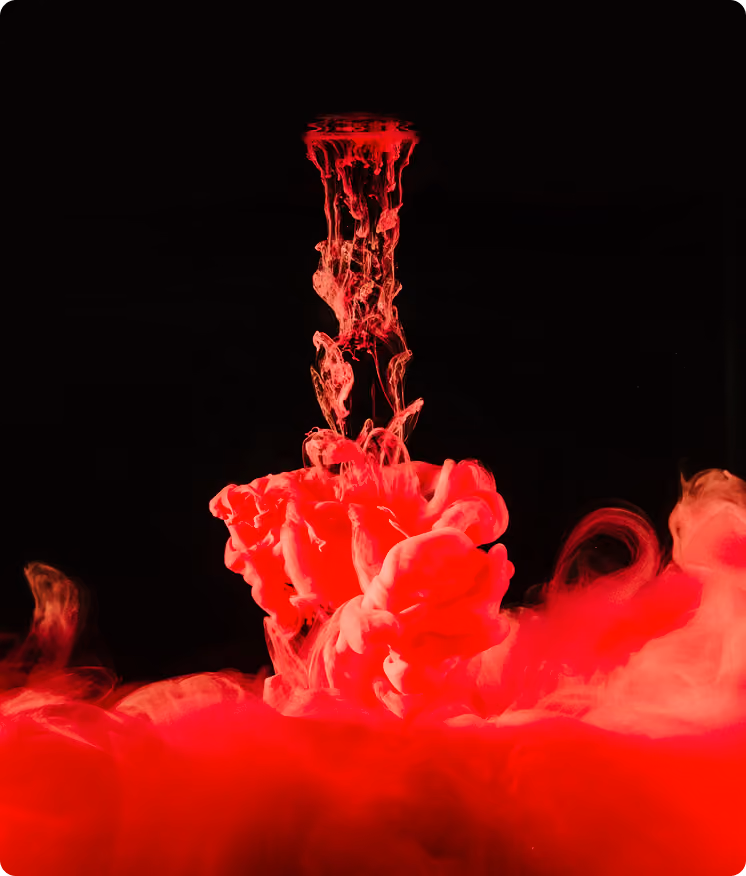 Bright red ink swirling and rising in dark water with intricate fluid shapes.