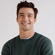 Smiling young man with dark hair wearing a green sweater against a plain background.