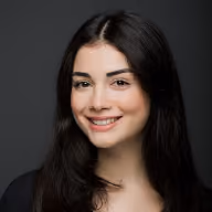 Smiling young woman with long dark hair in front of a dark background.