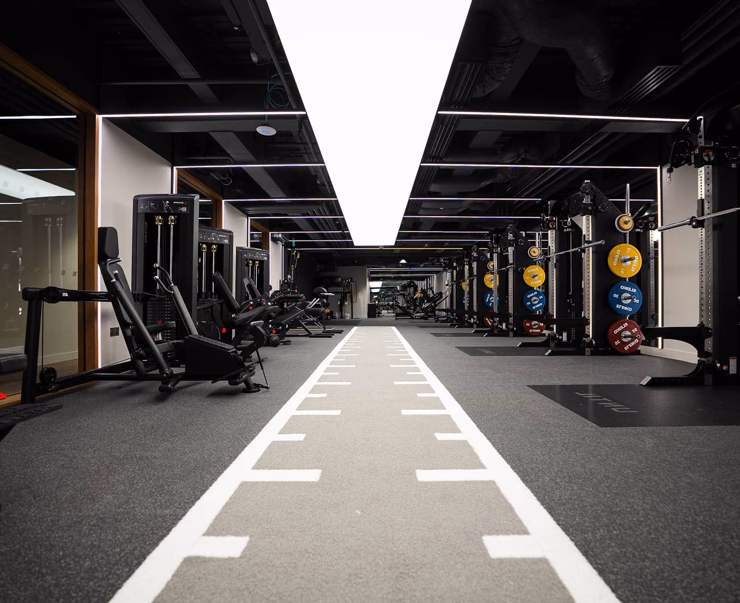 Modern gym with weight machines on the left and barbells with colorful plates on the right.