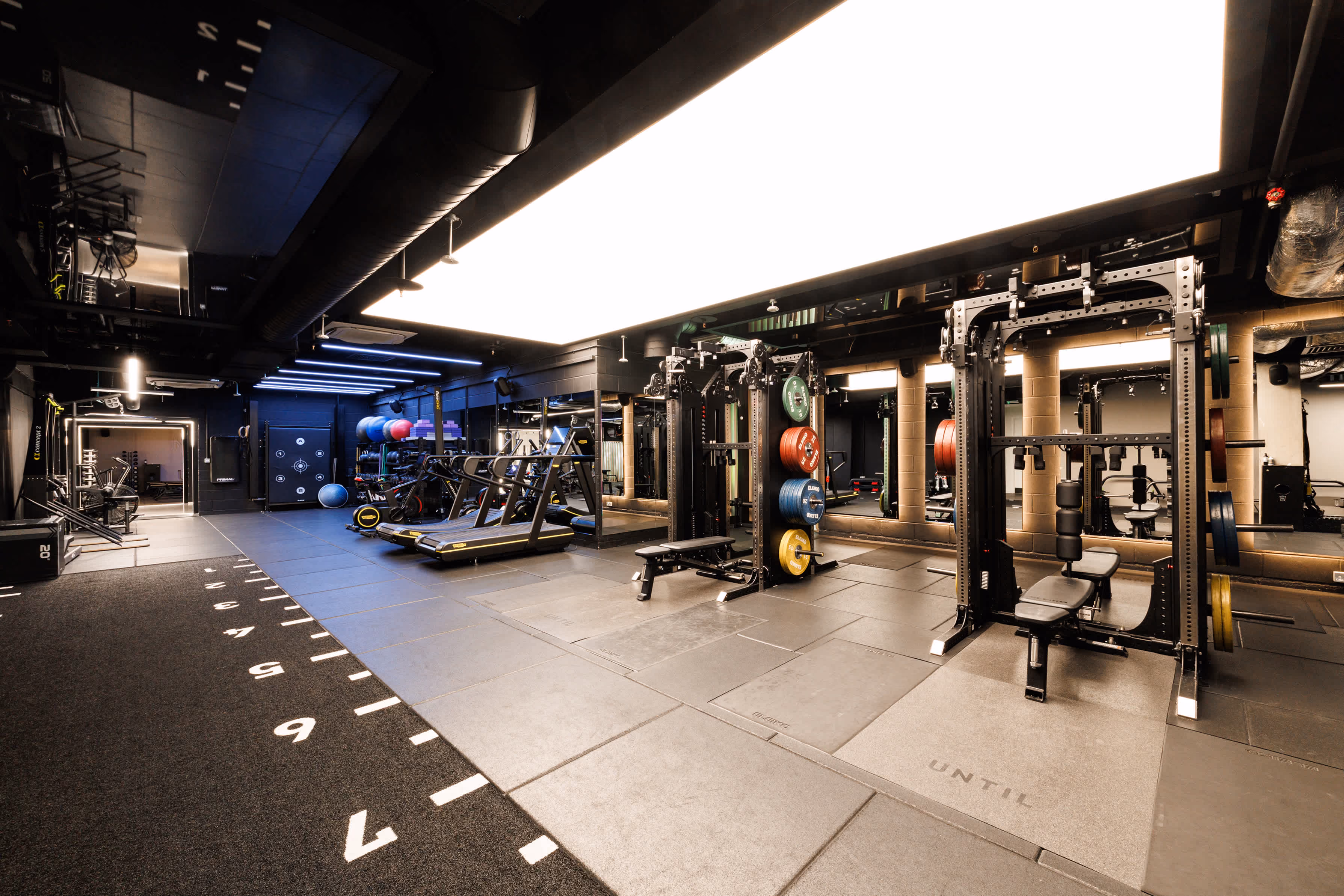 Modern gym with weight machines, treadmills, exercise balls, and rubber flooring with marked numbers.
