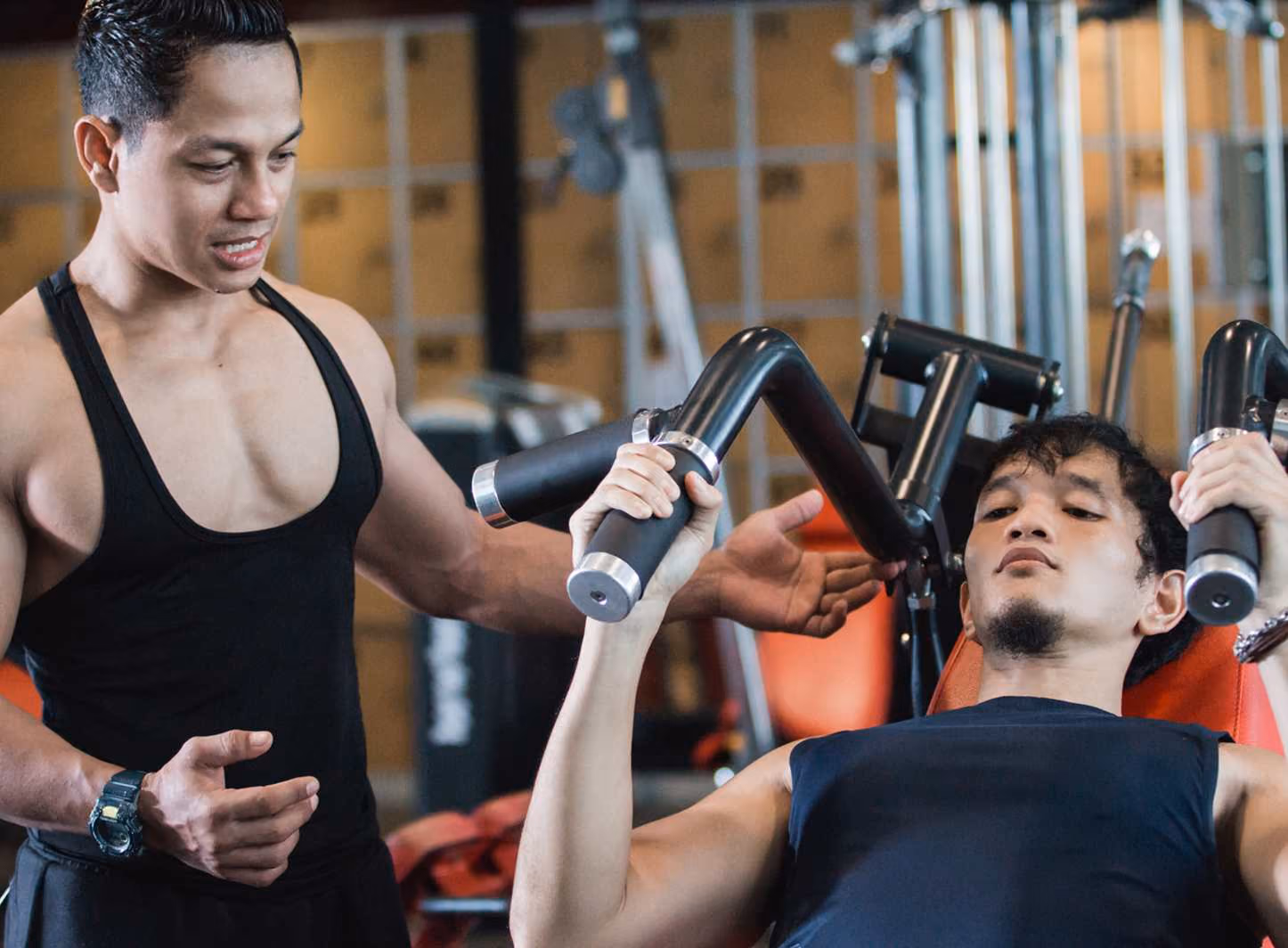Trainer guiding man using chest press machine in a gym.