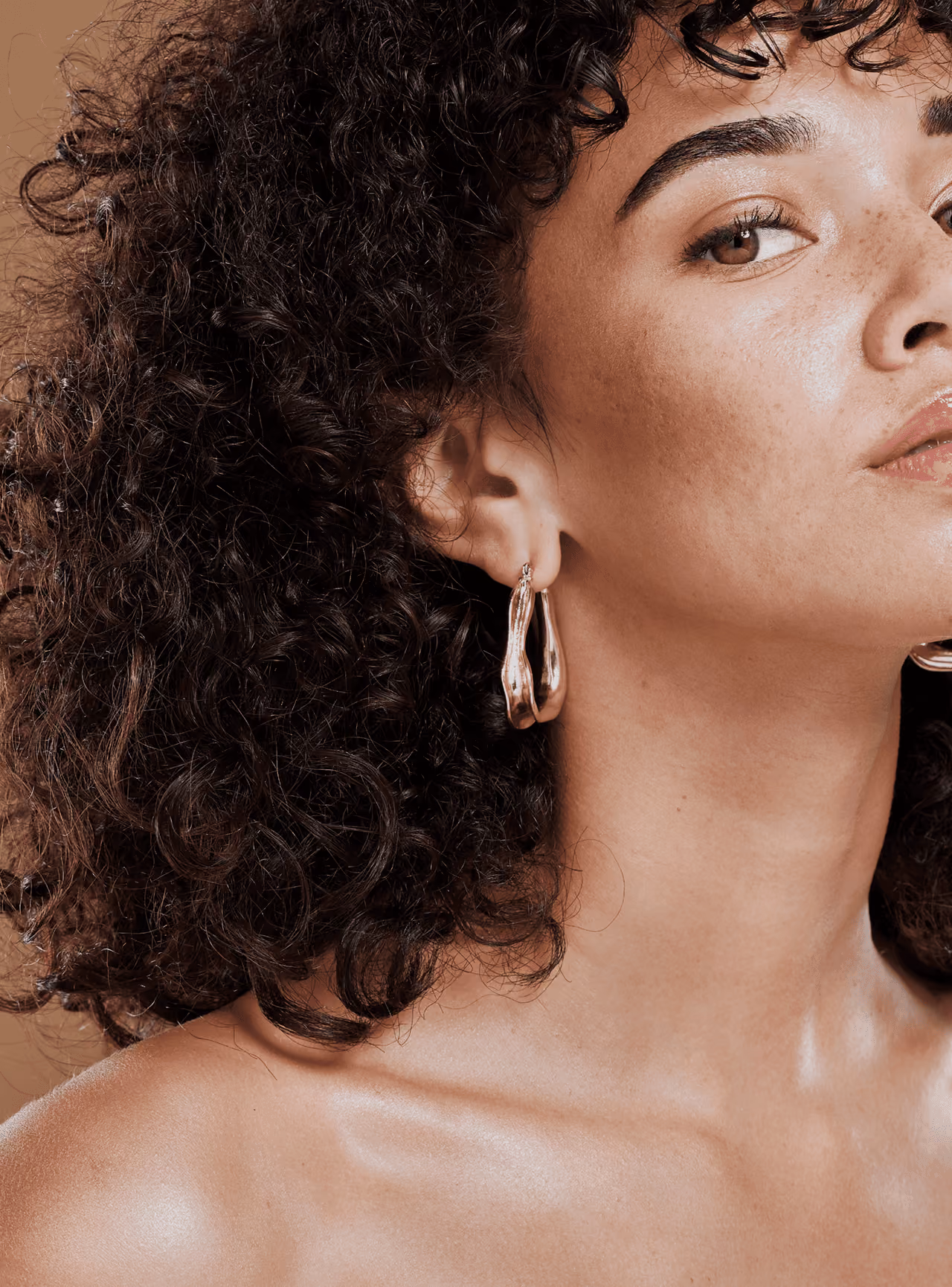 Portrait d’une femme aux cheveux bouclés portant une boucle d’oreille dorée, regard caméra