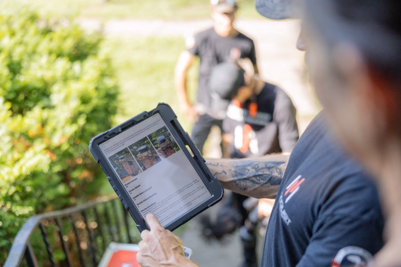 chimney technician holding a tablet displaying a chimney inspection report, with others blurred in the background.