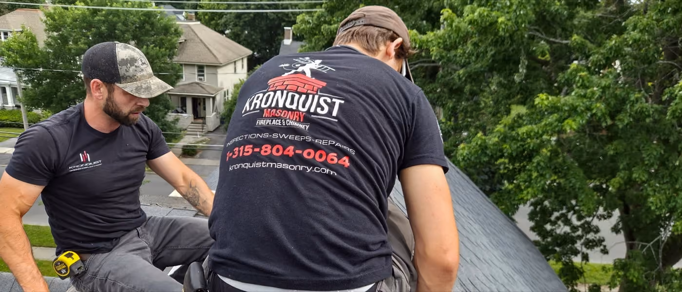 Two workers in black Kronquist Masonry shirts repairing closing up a chimney hole on a home rooftop.