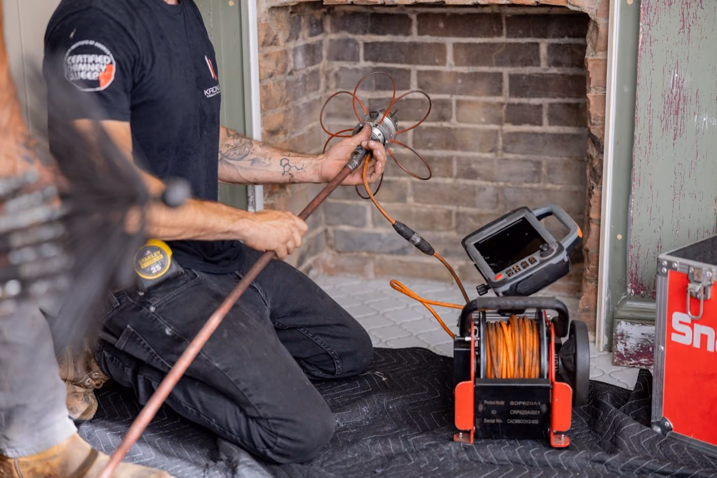 Person preparing a chimney inspection camera near a brick fireplace opening.