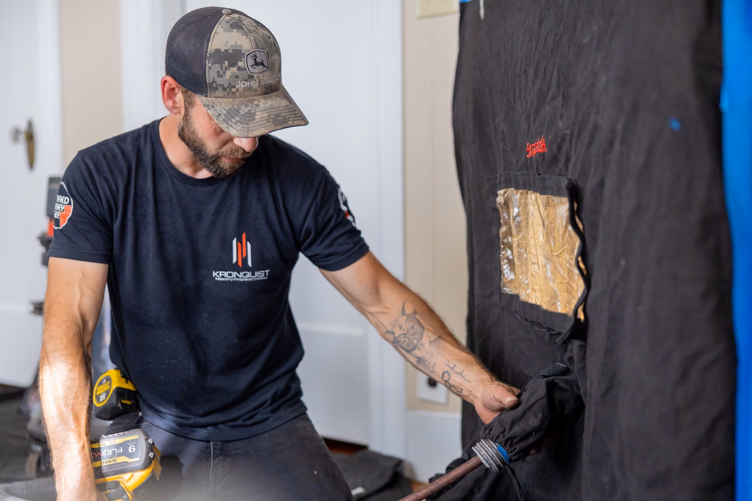 Chimney worker in a John Deere cap working with a power drill near a black insulated wall panel.