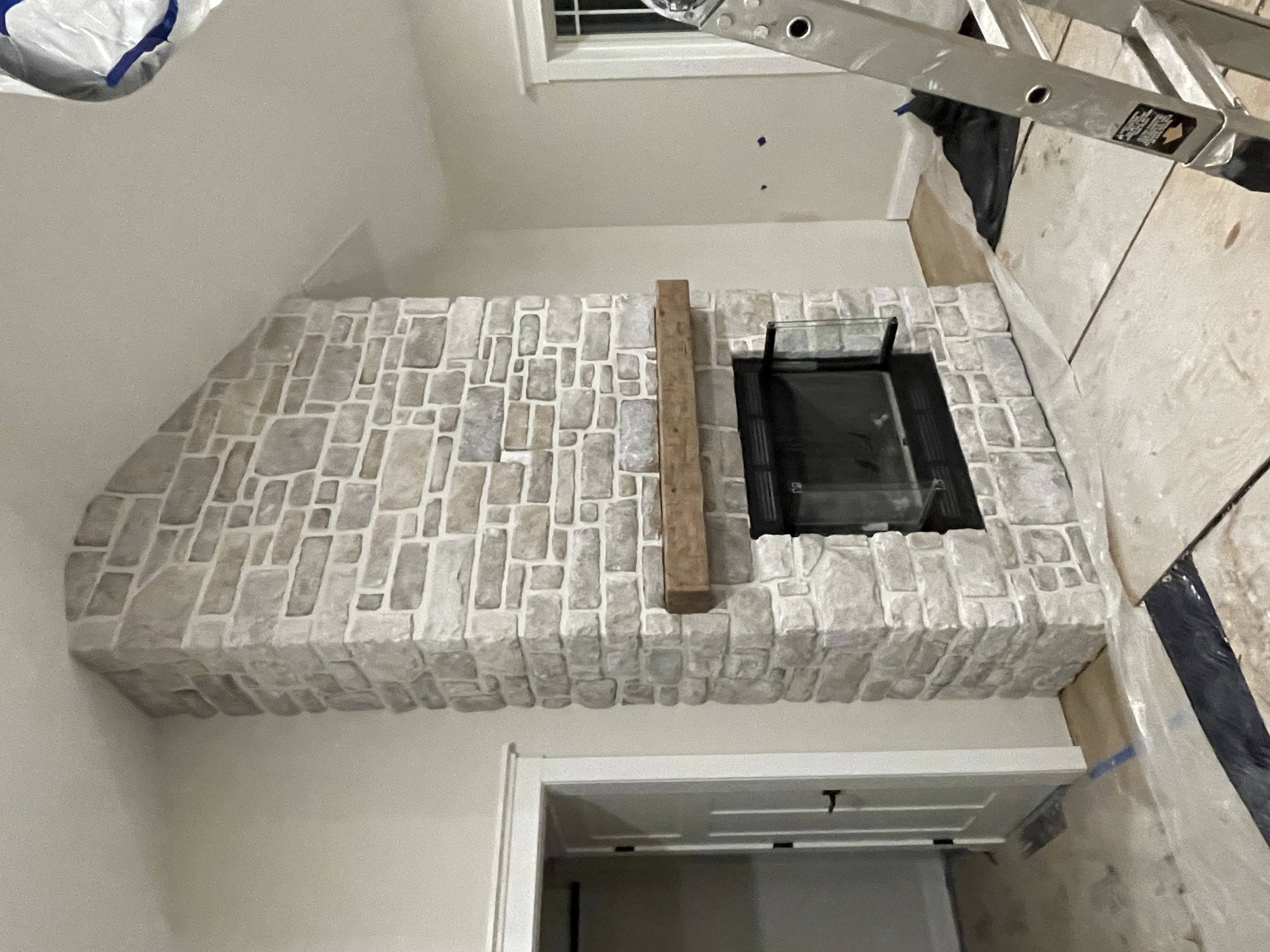 Stone fireplace with wooden mantle in a room under renovation with ladder and protective floor coverings.