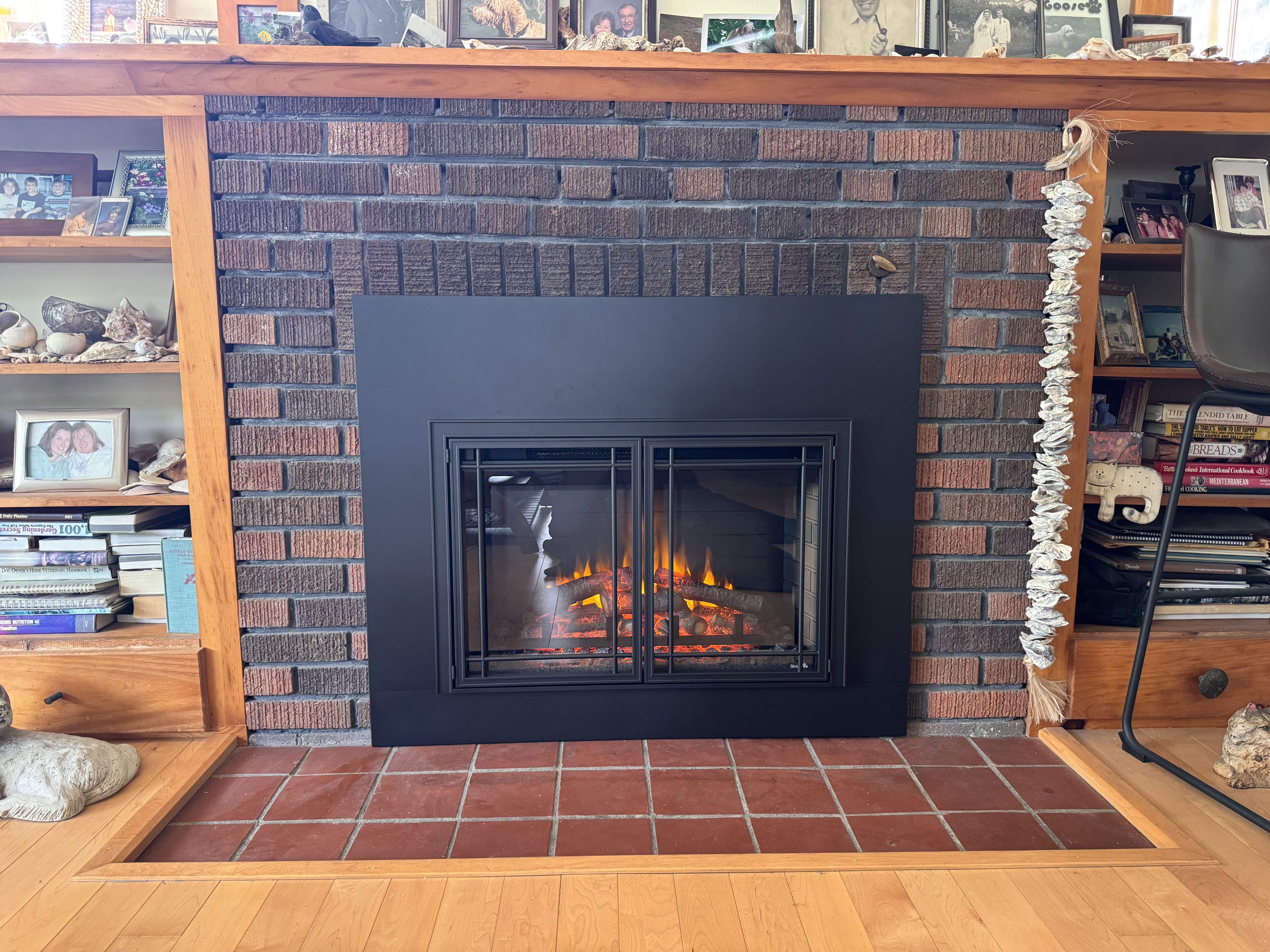 Brick fireplace with black metal frame and glass doors, with flames and logs inside.