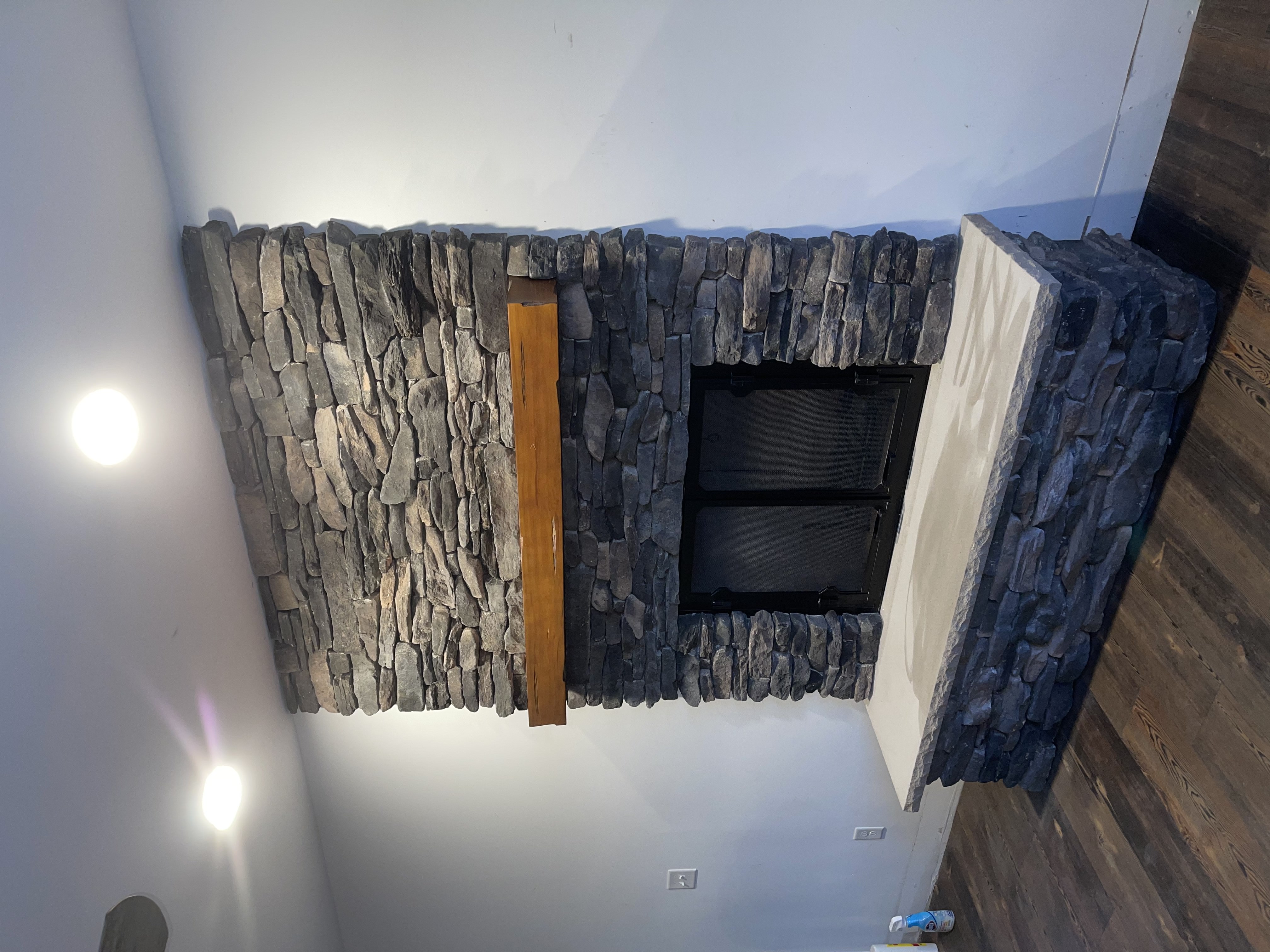 Stone fireplace with wooden mantel and a concrete hearth in a room with wooden floor.