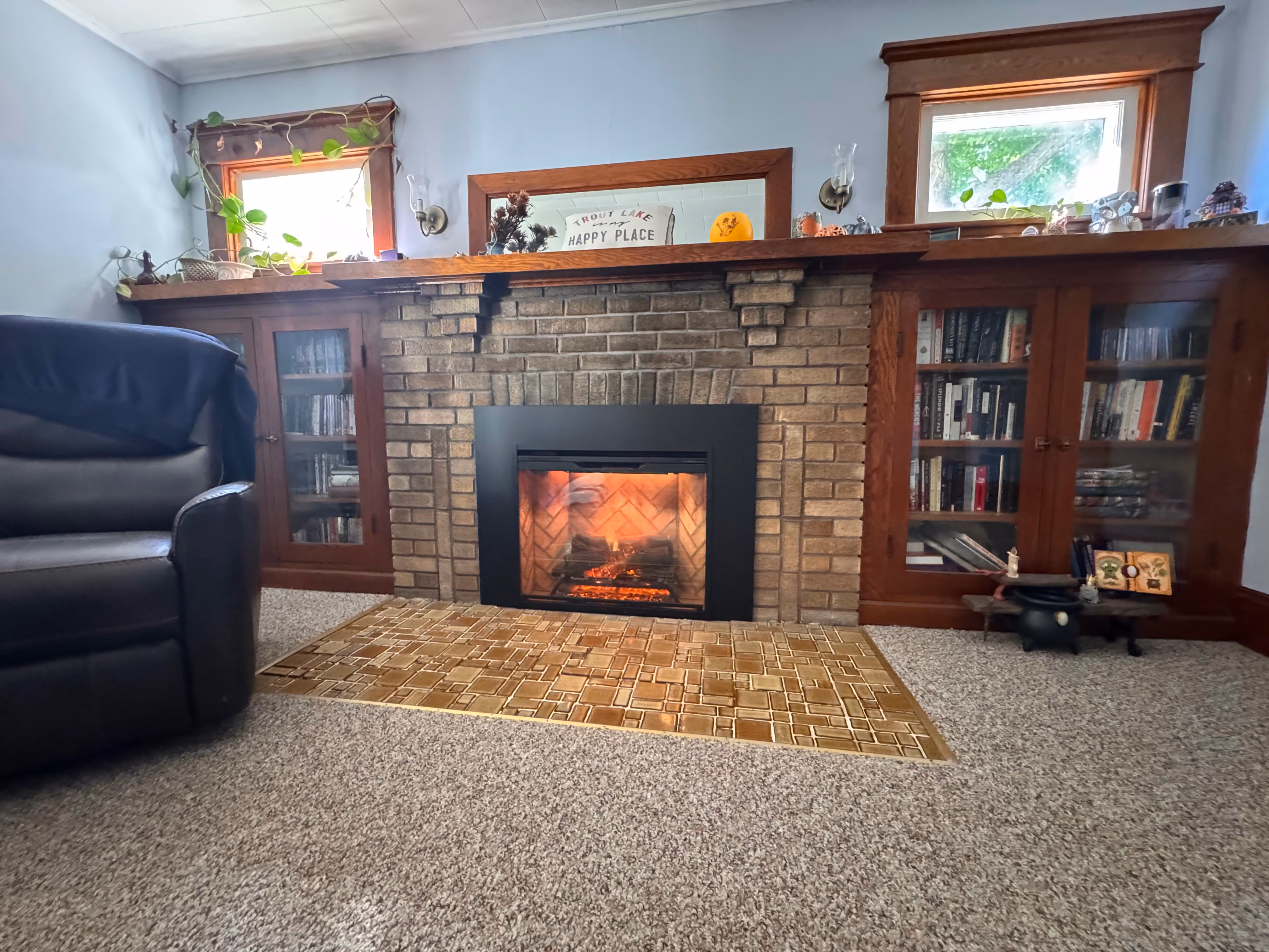 Cozy living room with a burning fireplace flanked by wooden cabinets filled with books and decor.