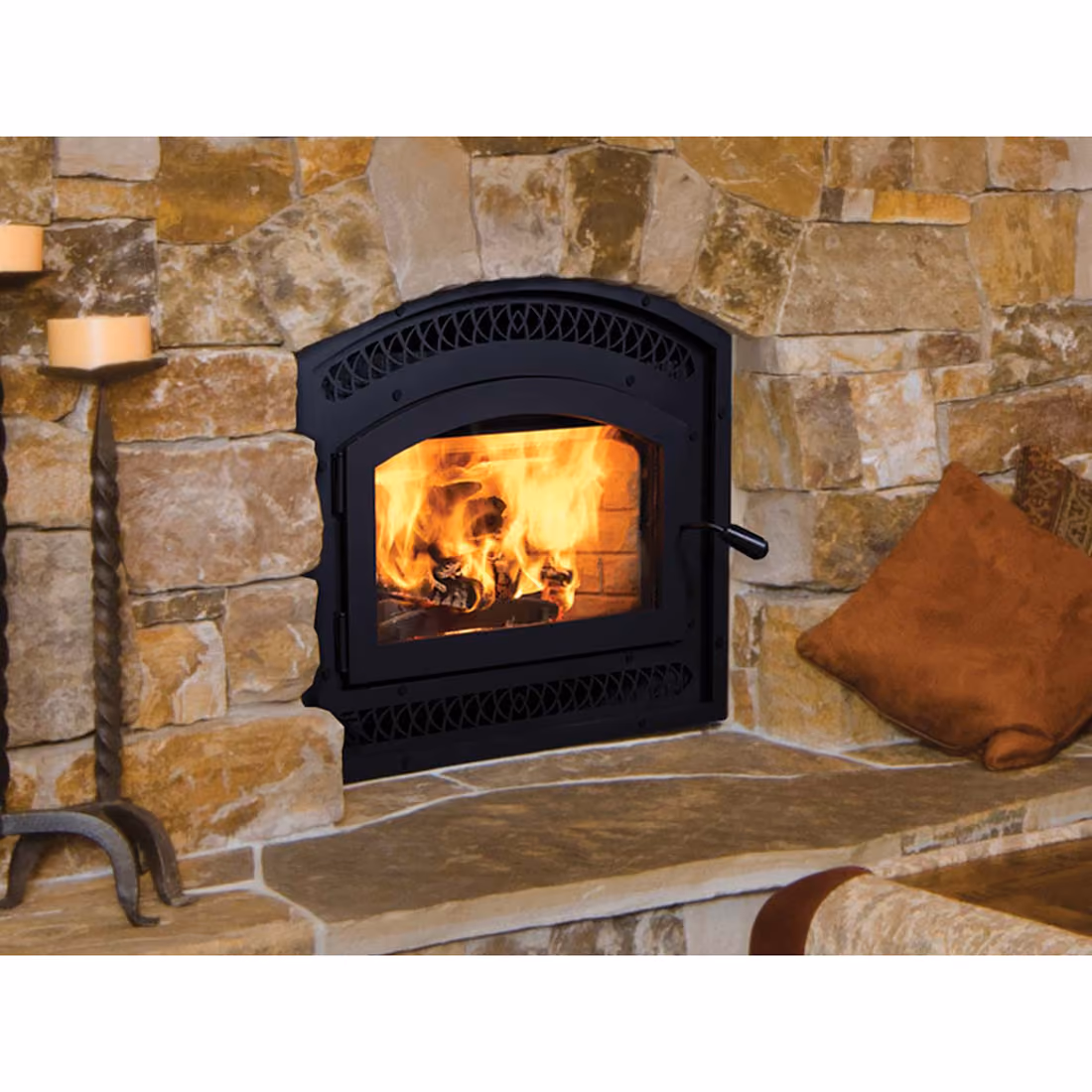 Black metal wood-burning stove with fire inside set in a stone fireplace with cushions nearby.