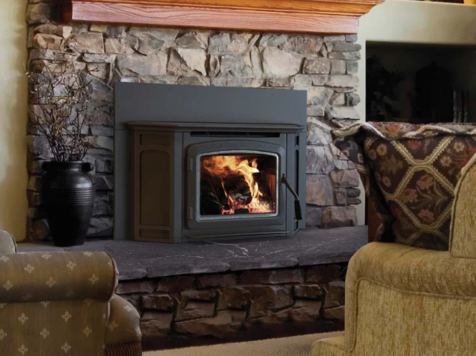 Black wood-burning stove with fire inside set in a stone fireplace surrounded by cozy furniture.