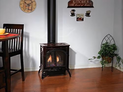 Lit black wood stove on wooden floor near dining chair with kitchen wall decor above.