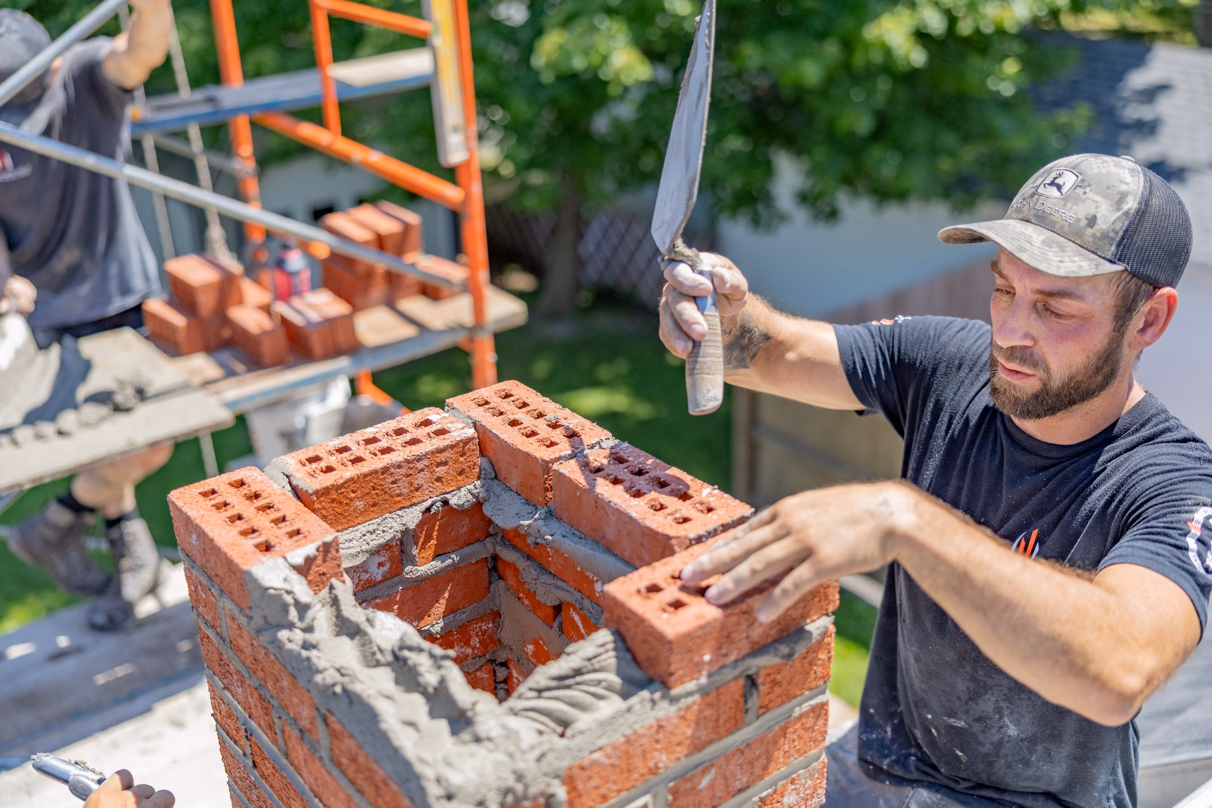 Two chimney workers repairing a brick chimney on a rooftop with safety harnesses and tools.