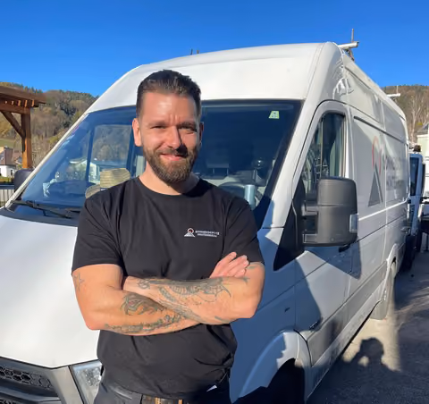 Mann mit Tattoos posiert vor weißem Lieferwagen bei sonnigem Wetter.